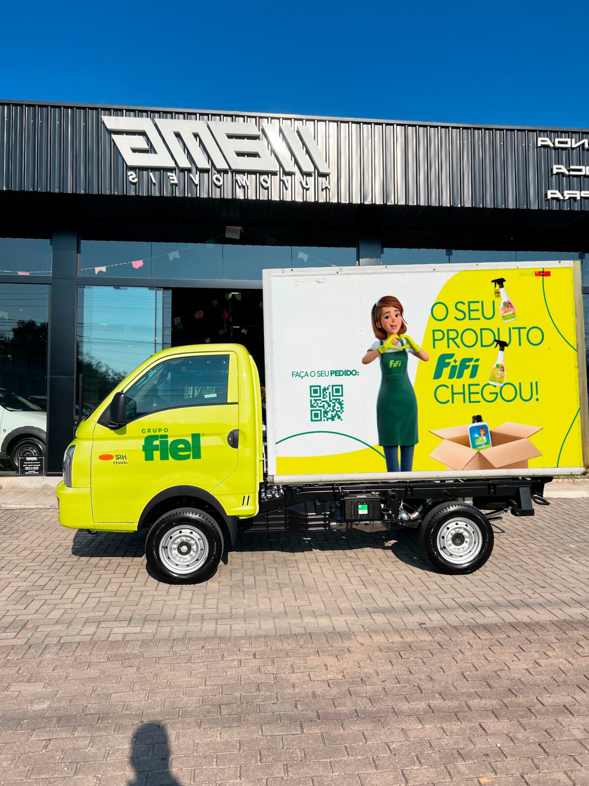 Caminhão baú FIFI com a mensagem O seu produto FIFI chegou em frente à loja, usado na logística própria
